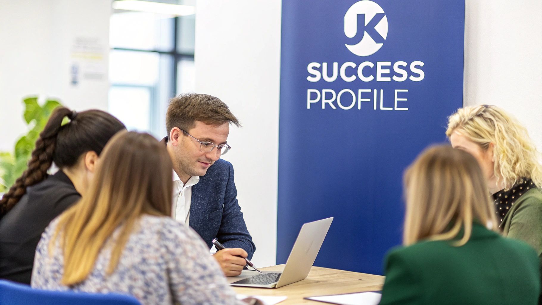 A group of professionals collaborating at a table with a laptop and a recruitment banner.